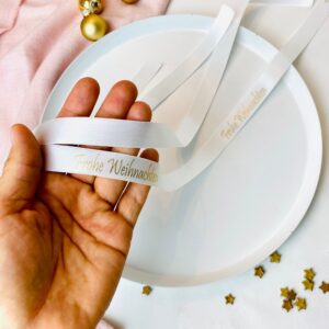 weißes Geschenkband, Satinband in der Hand mit Aufdruck in gold Frohe Weihnacht